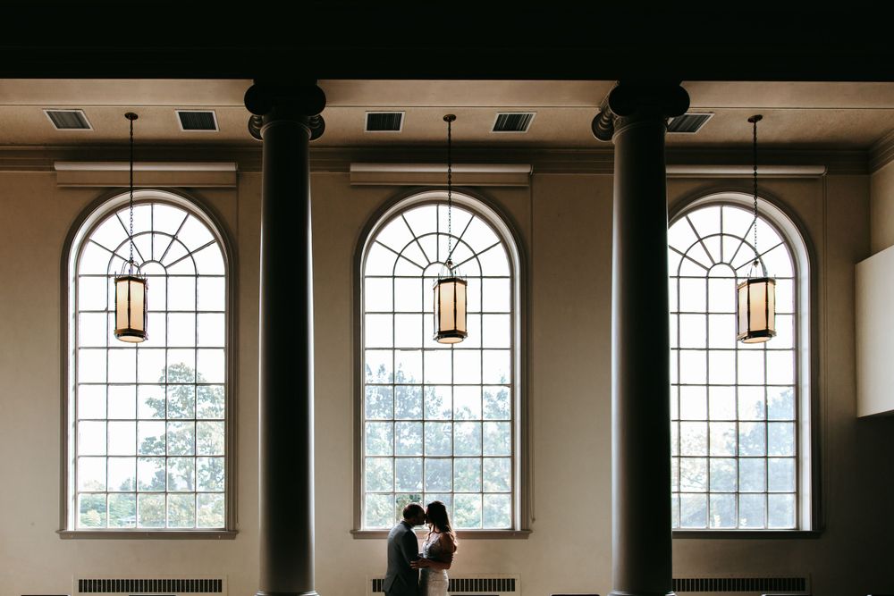 Intimate moment captured in church with grand arched windows and columns creating dramatic lighting.