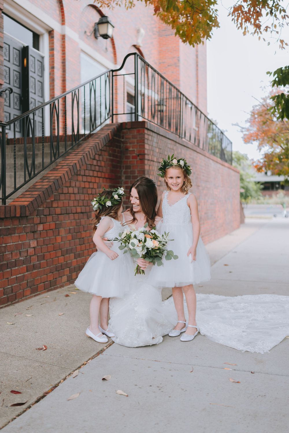 A wedding scene on brick steps with white dresses and floral arrangements in autumn.