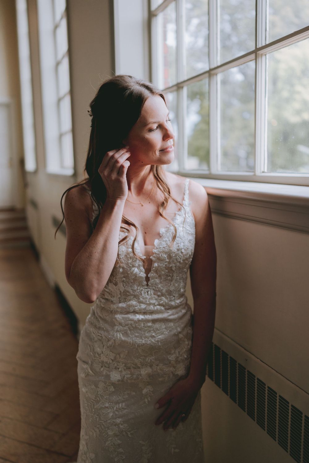 A detailed lace wedding dress is showcased near a bright window.