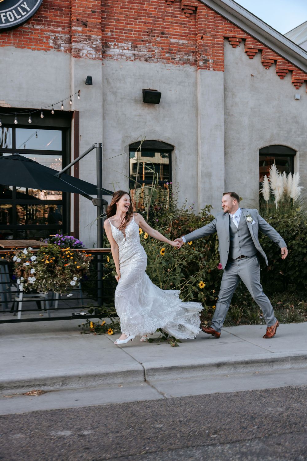 A playful moment between newlyweds dancing outside a historic brick building with string lights.