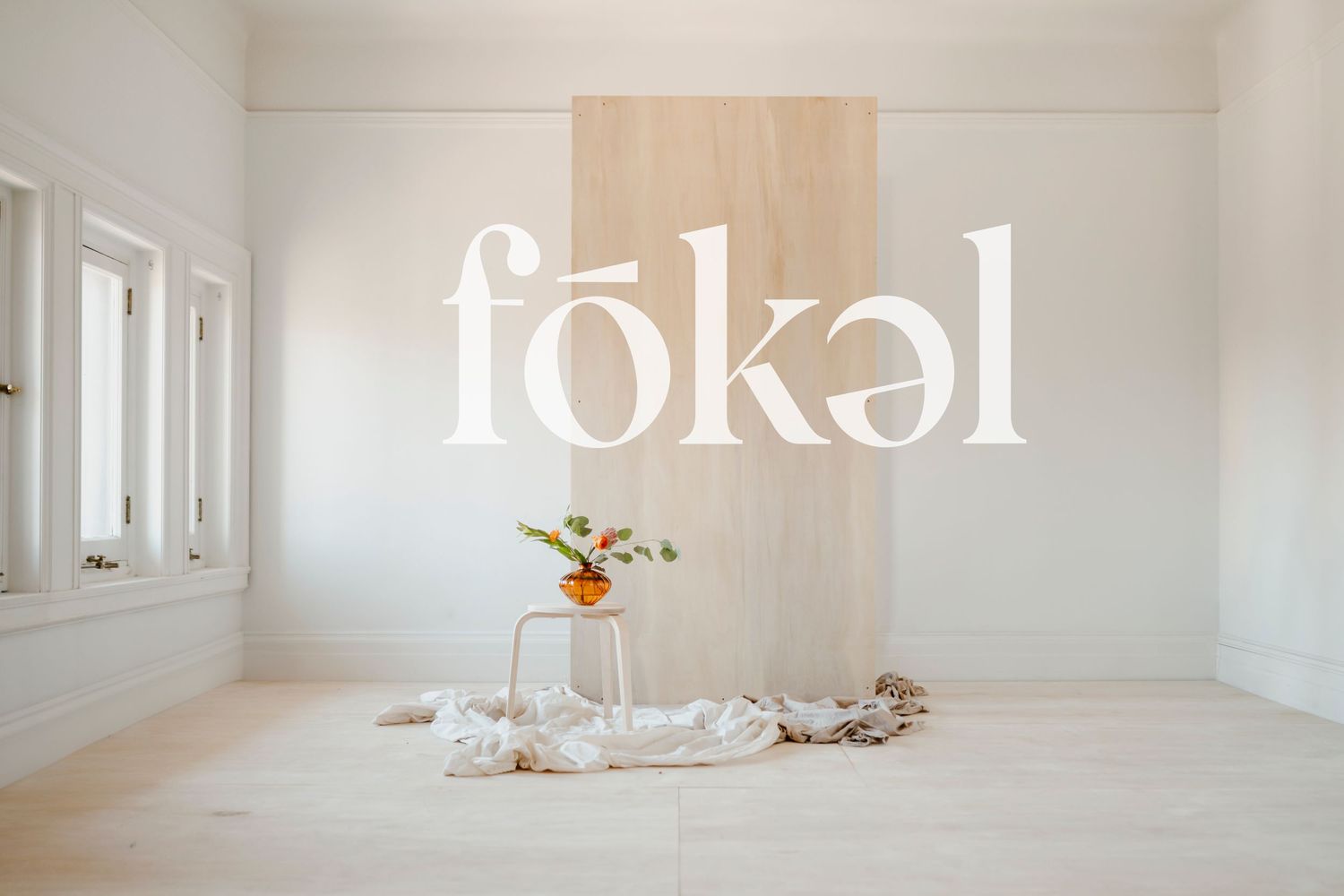 Minimalist white text spelling 'fokal' on light beige wall with floral arrangement.