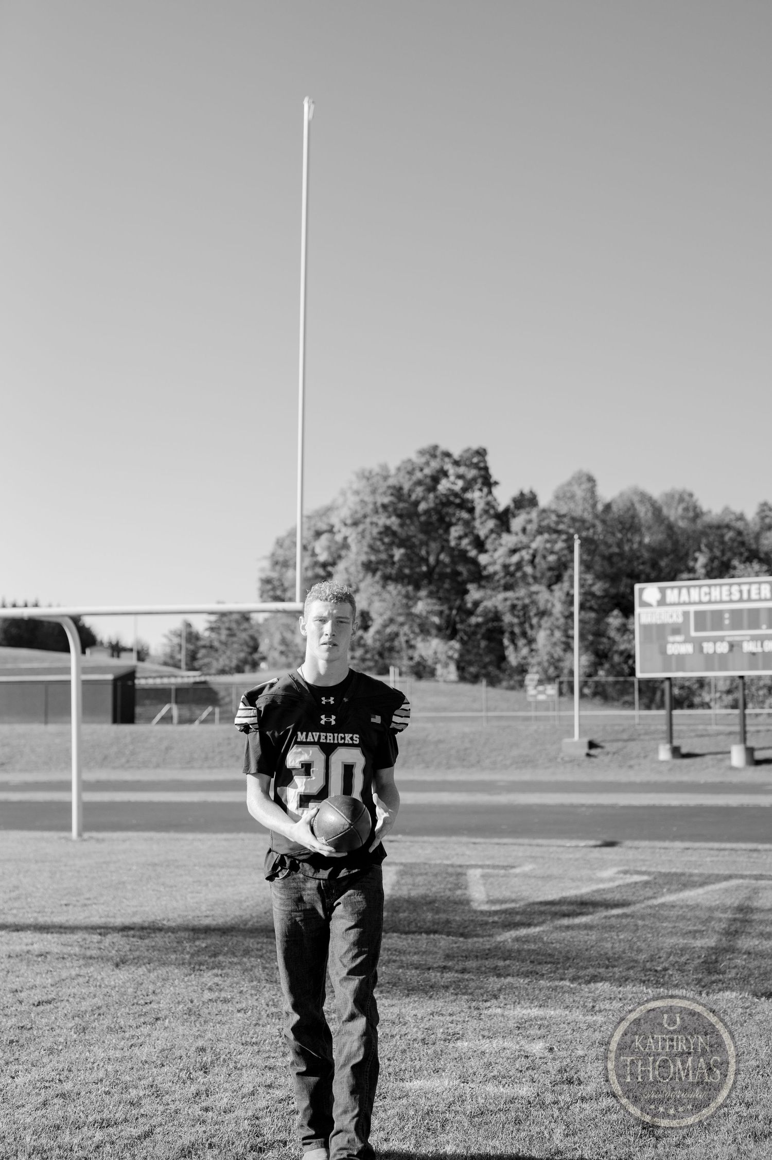 A player in a number 20 Mavericks jersey stands on a football field with goalposts and scoreboard visible.