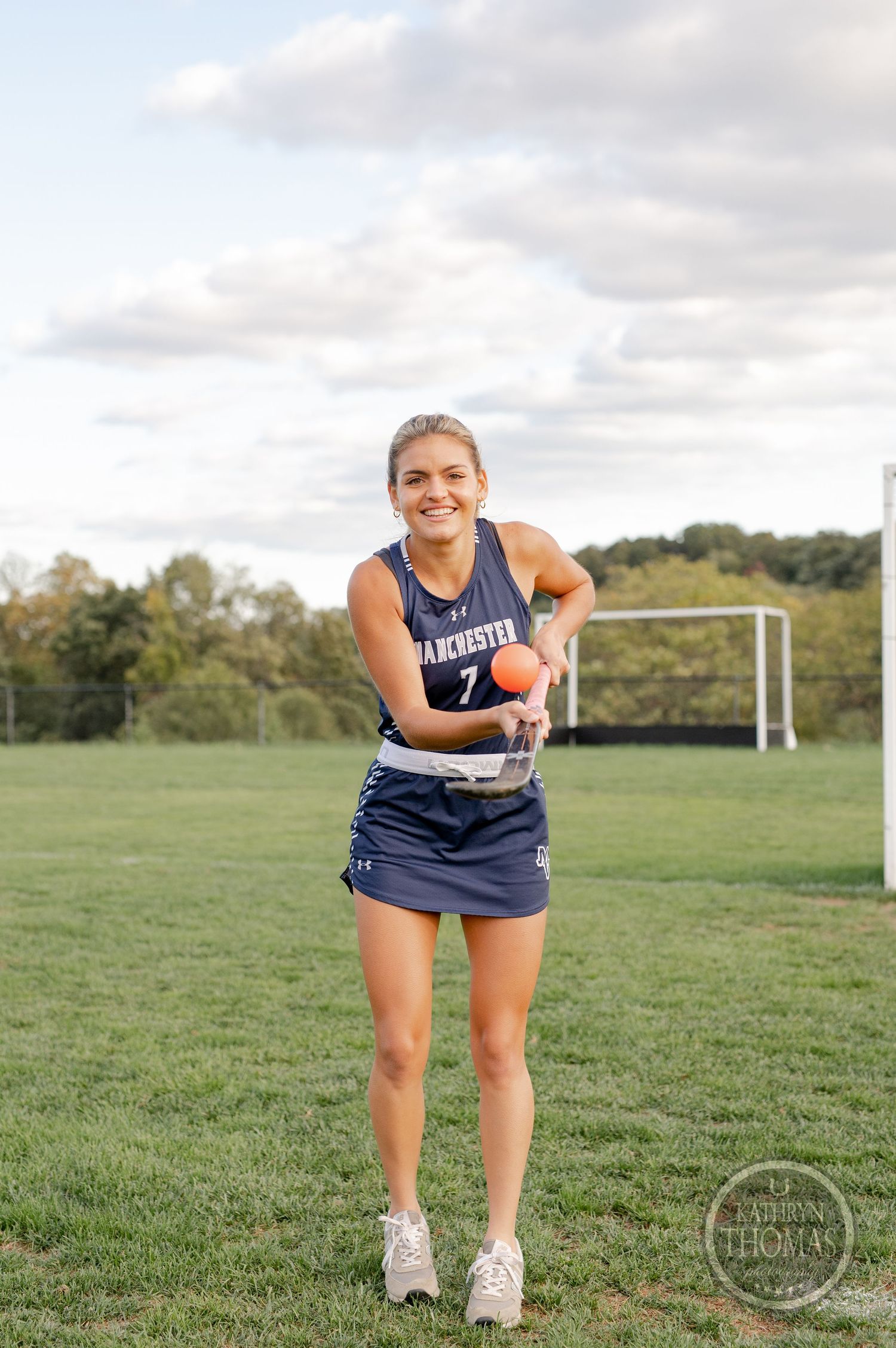 Athlete in Manchester Valley navy uniform stands on field hockey pitch with stick.