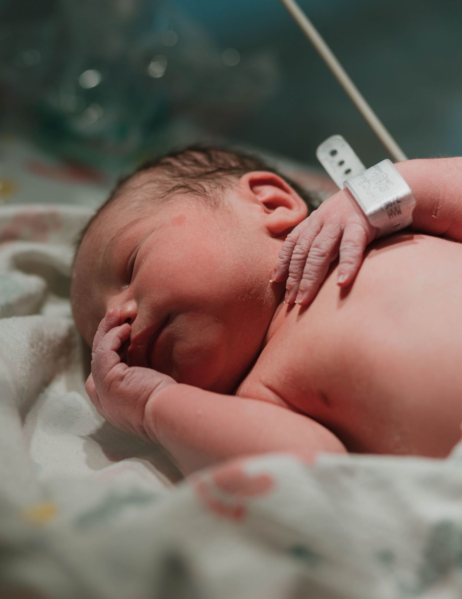 A newborn baby rests peacefully on a hospital bed with a medical ID bracelet visible.