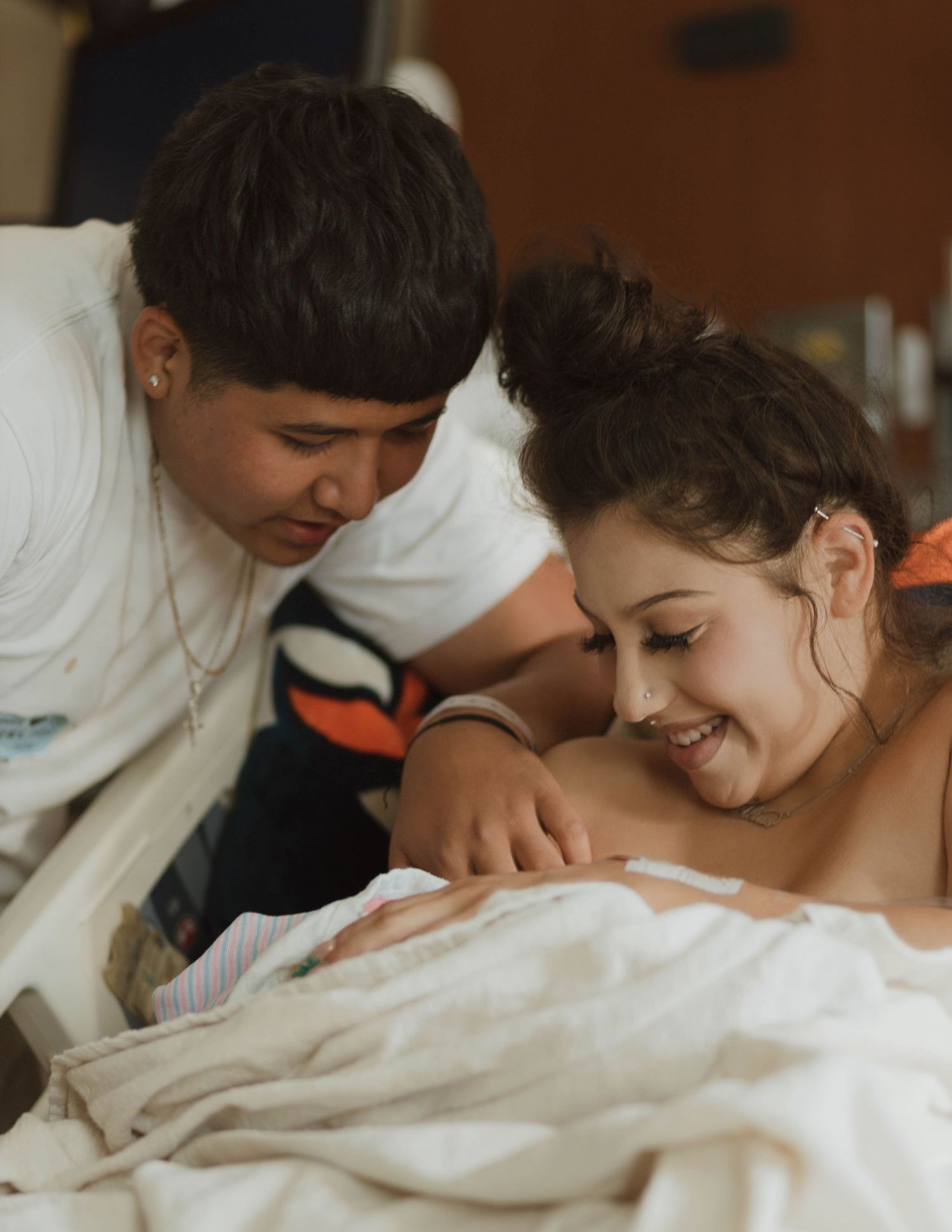 A tender moment in a hospital room as family members gaze lovingly at a newborn baby wrapped in white blankets.
