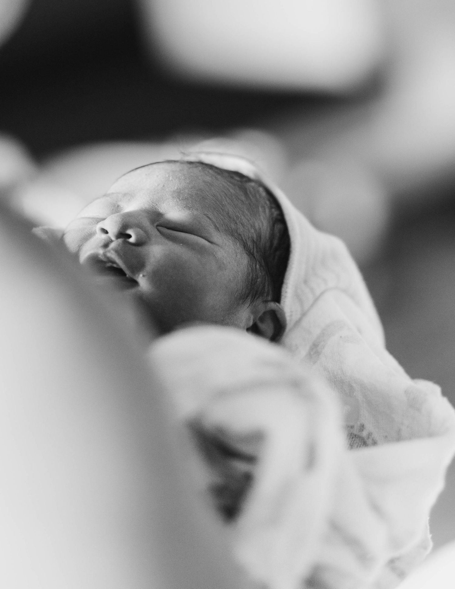 Black and white close-up portrait of a newborn baby wrapped in white blankets.