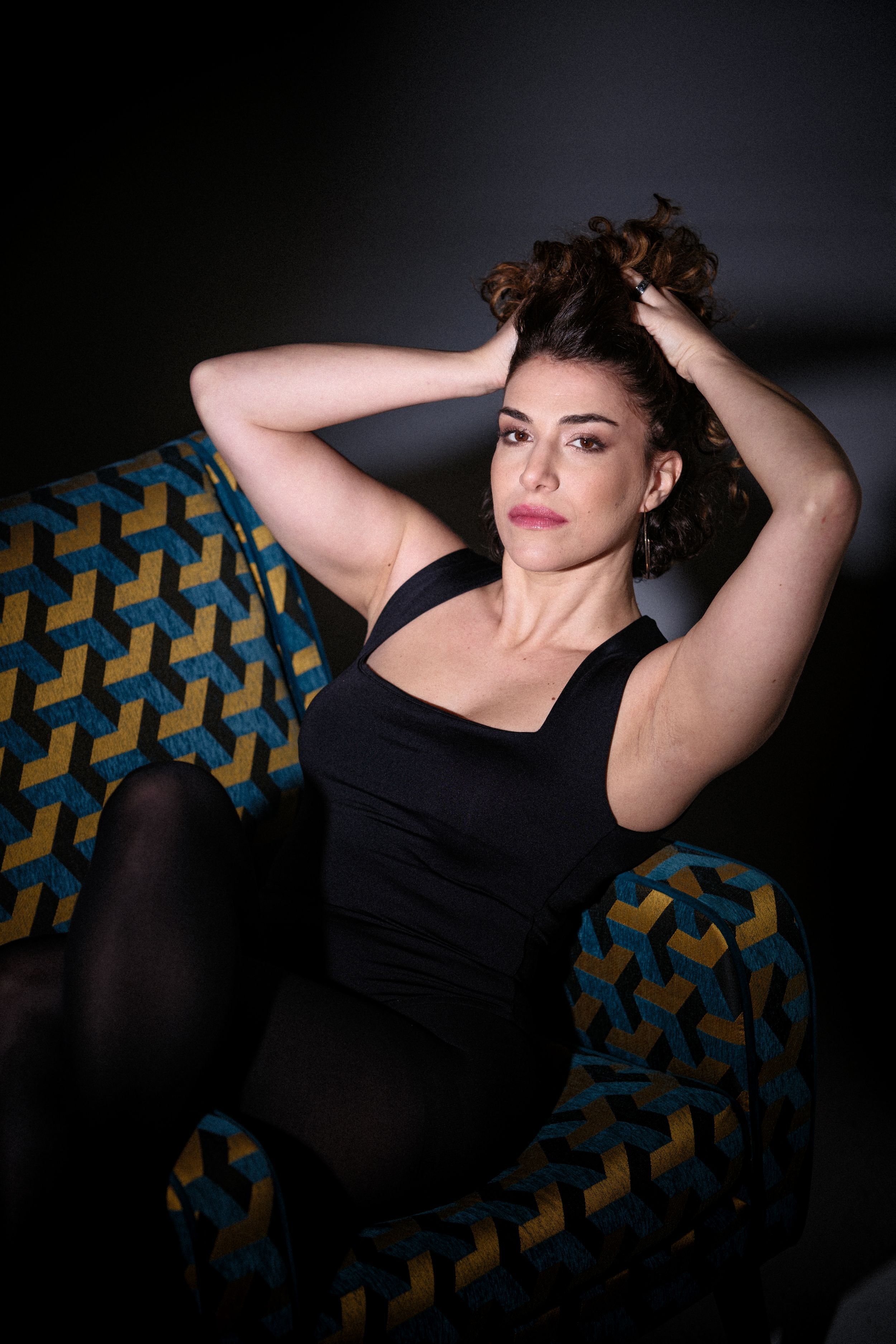 Moody boudoir portrait on patterned couch with dramatic lighting.