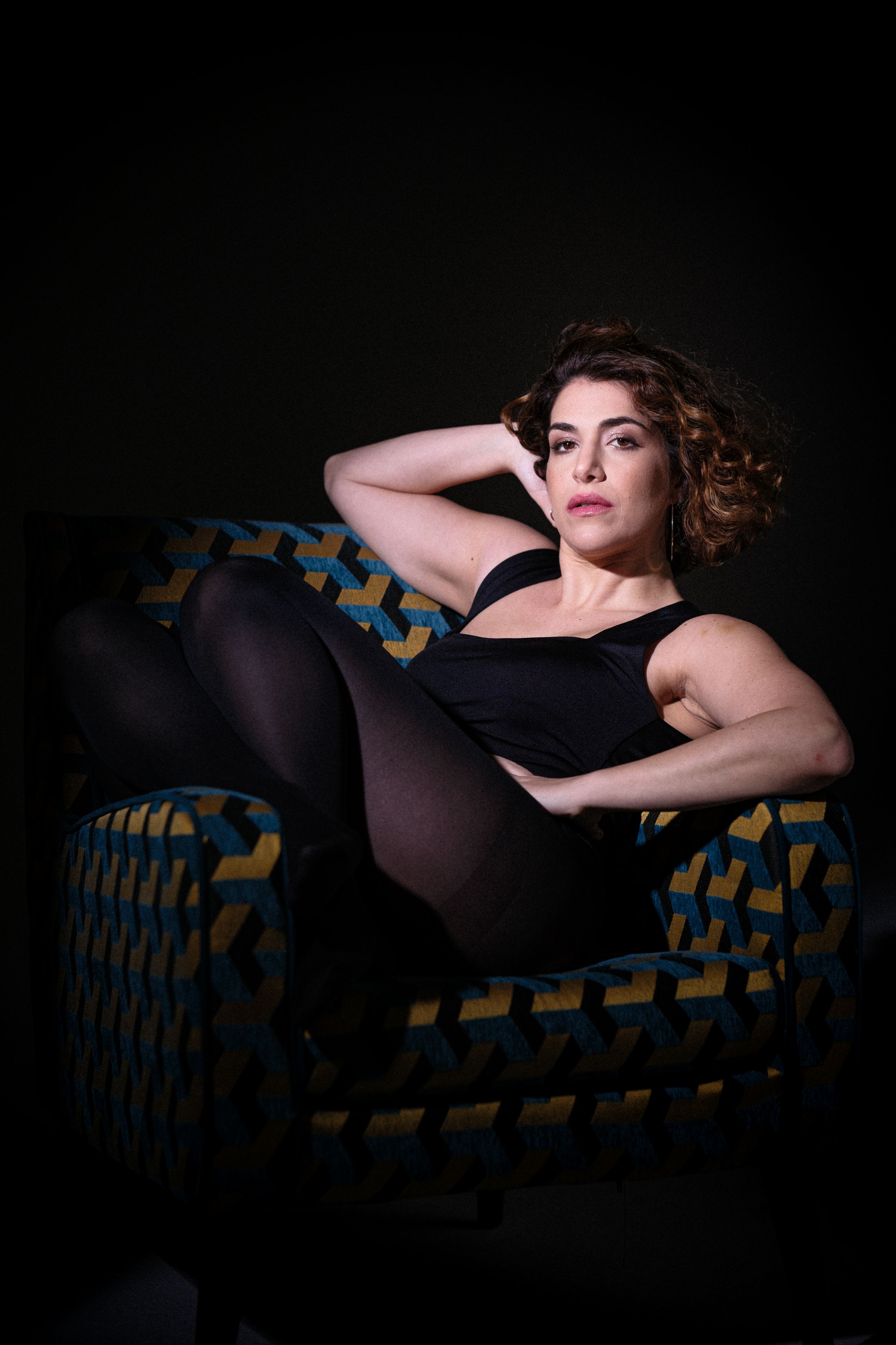 Film noir style portrait on geometric patterned couch in dark lighting.