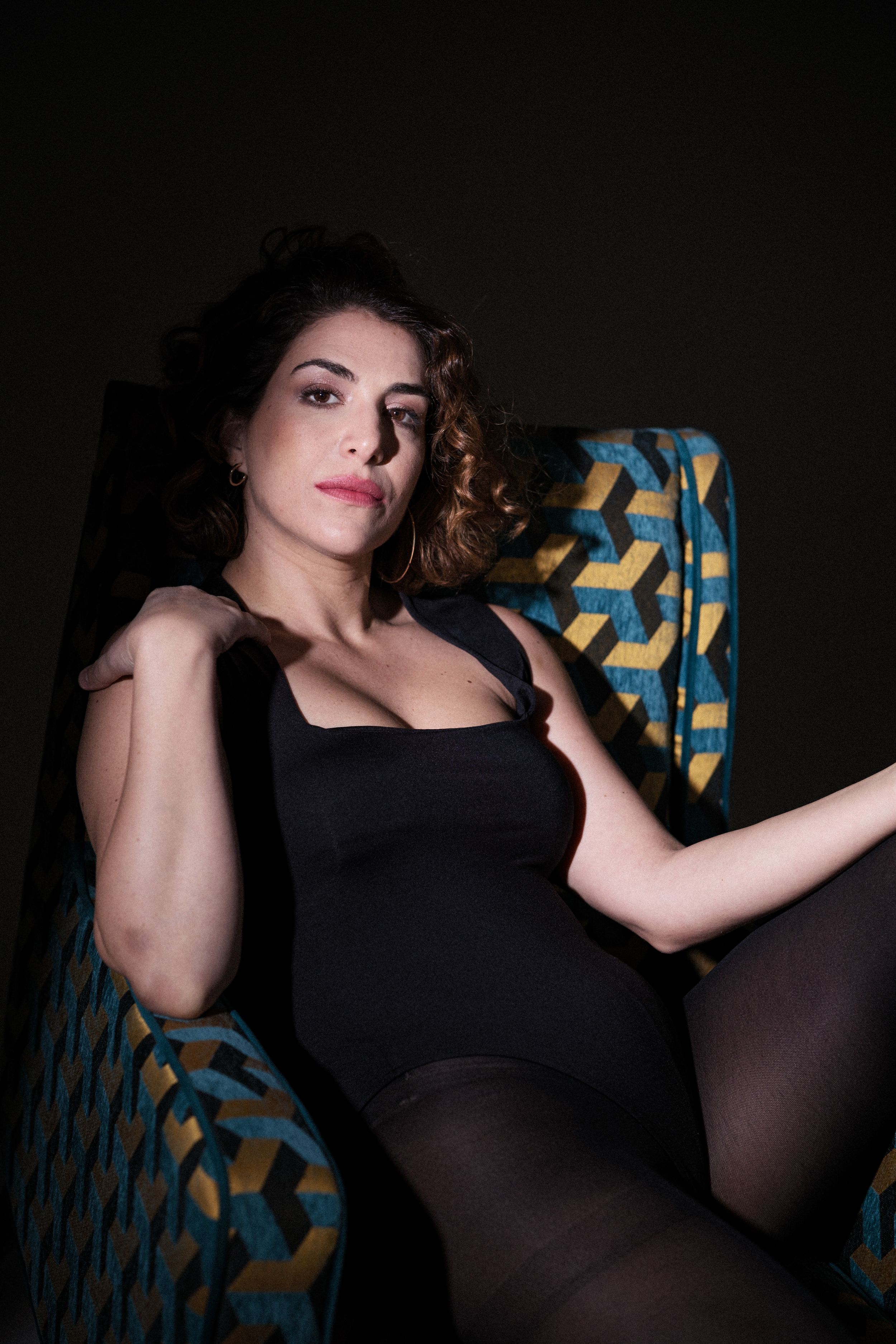 Artistic boudoir photography with geometric pattern furniture in dark setting.