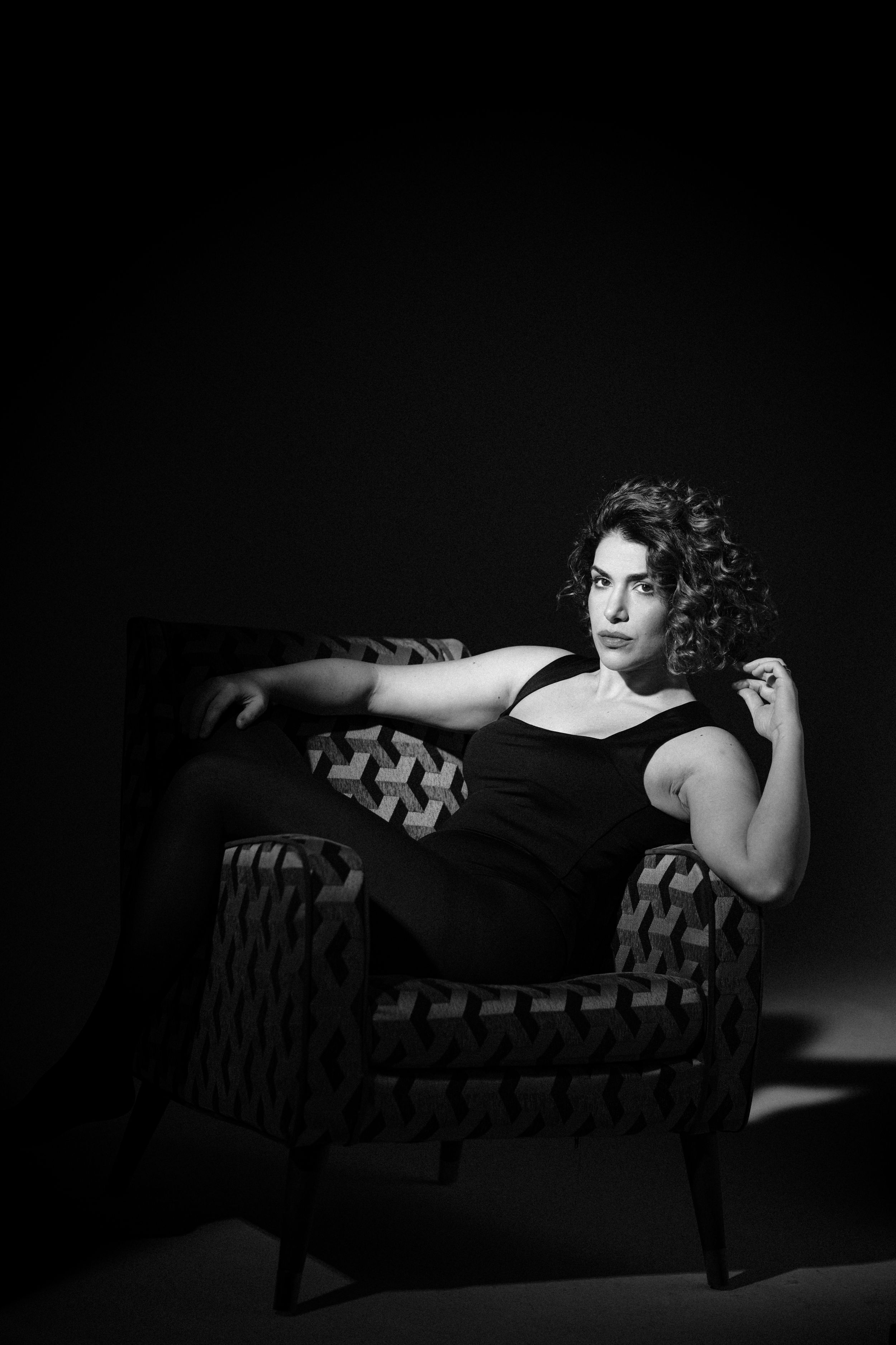 Black and white boudoir photograph showing figure lounging on vintage patterned chaise.