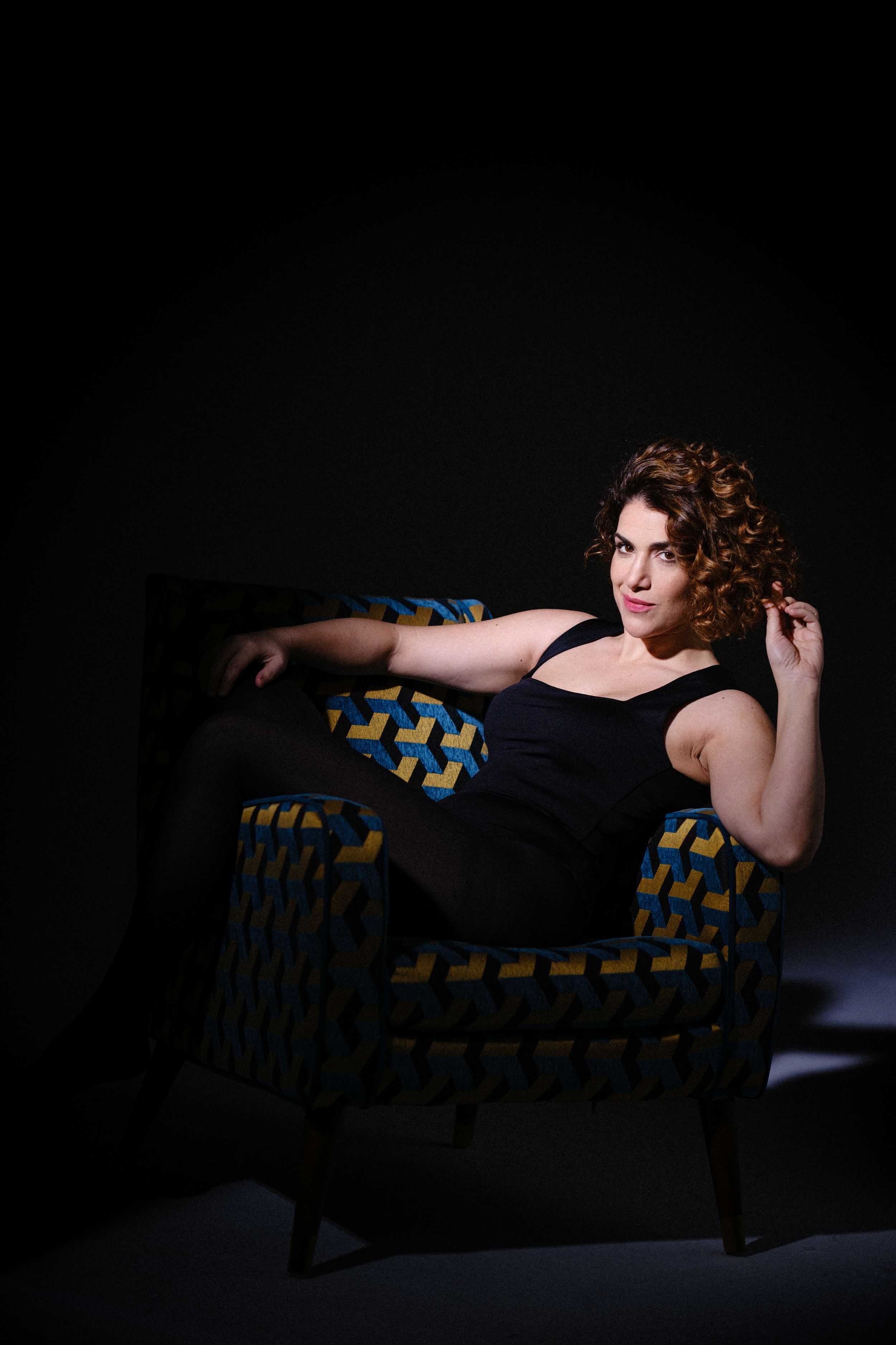 Dramatic studio portrait with figure in black dress posed elegantly on patterned couch.