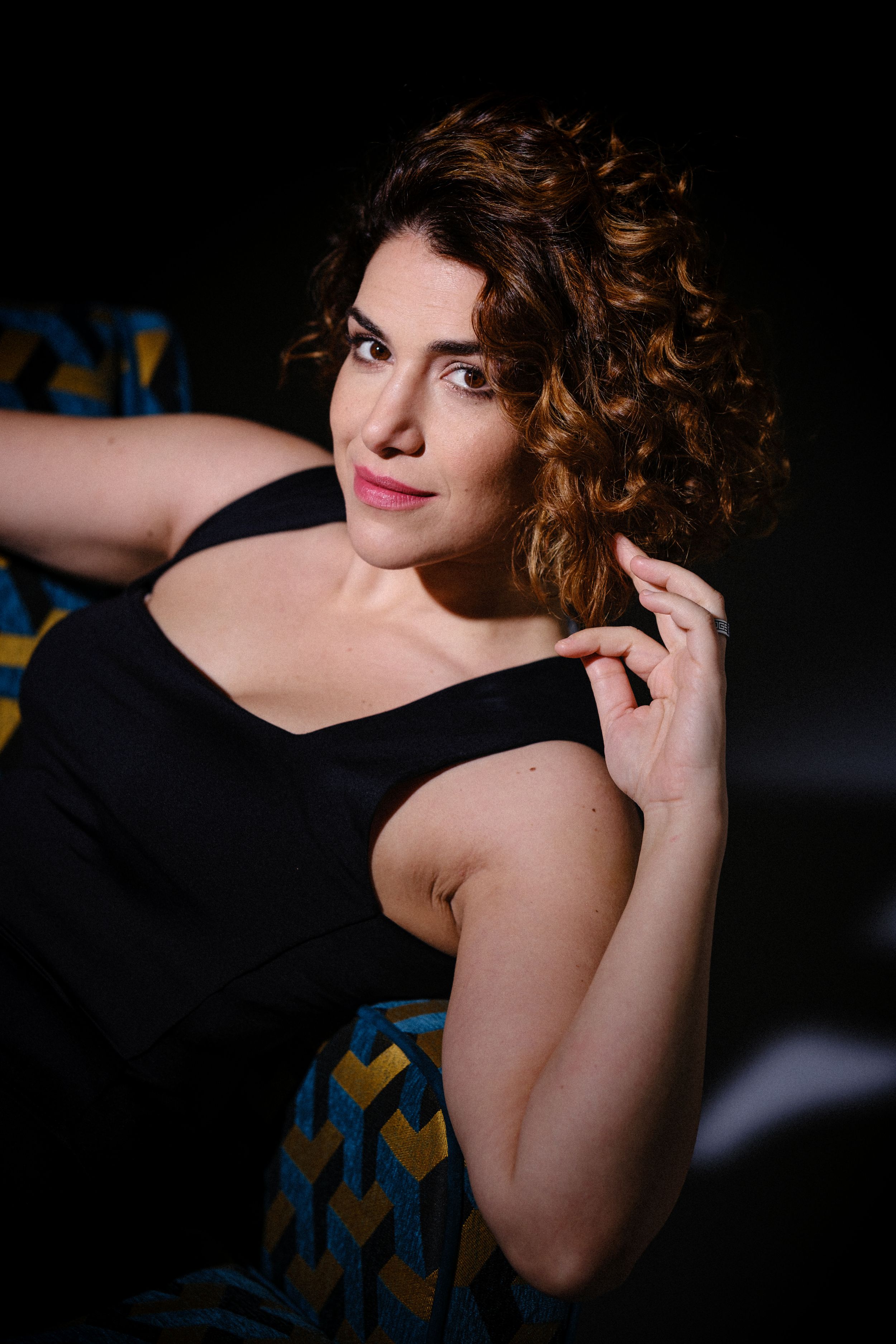 Intimate portrait with soft lighting highlighting curves against geometric patterned furniture.