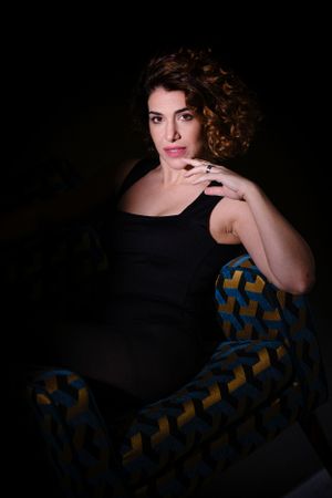 Atmospheric portrait with figure in black against blue and gold patterned chair.