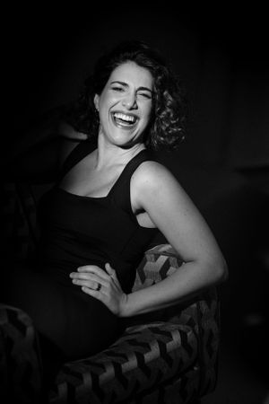 Candid black and white portrait capturing genuine laughter while seated in a patterned armchair.