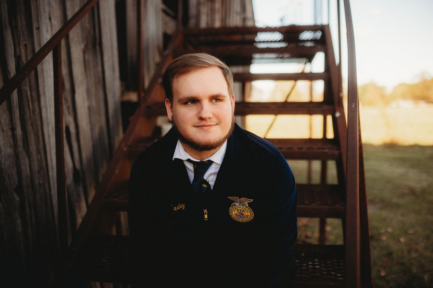 Senior boy sitting on metal steps next to a barn