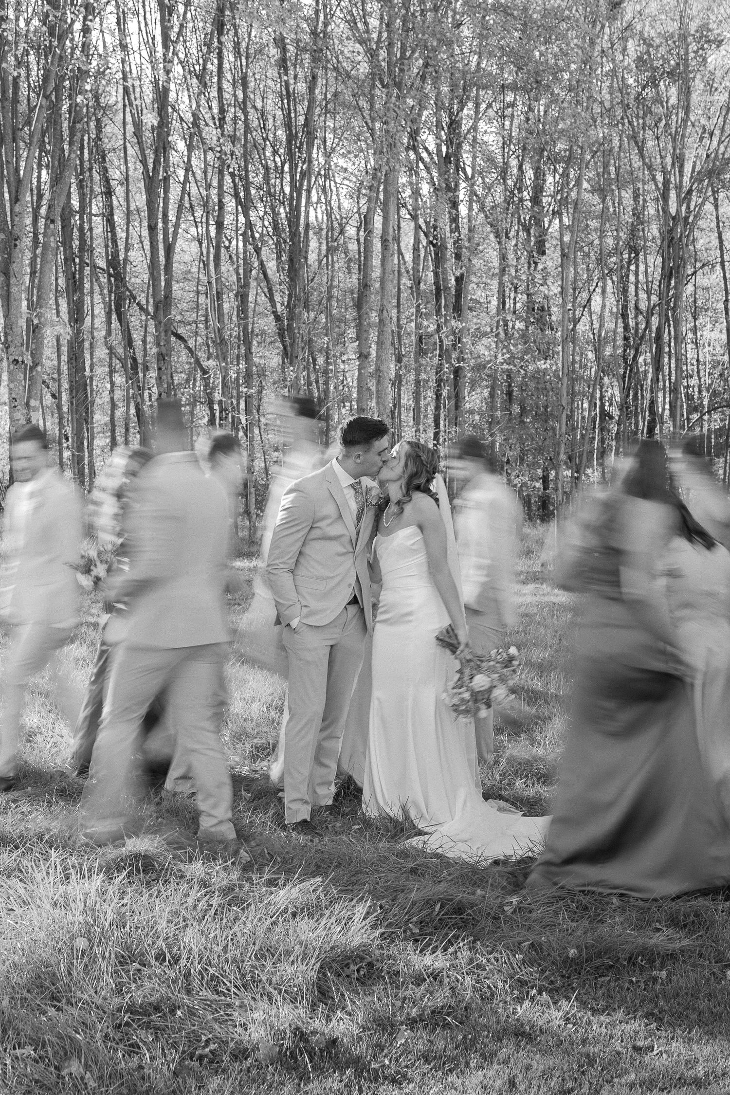 Artistic motion blur photograph of wedding party in a wooded setting creating an ethereal effect.