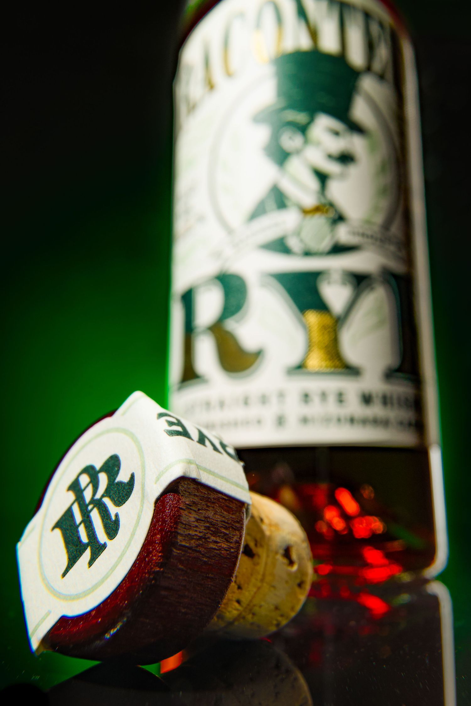 A Raconteur Rye bottle and cork displayed against a dark background with dramatic green lighting and red reflections.