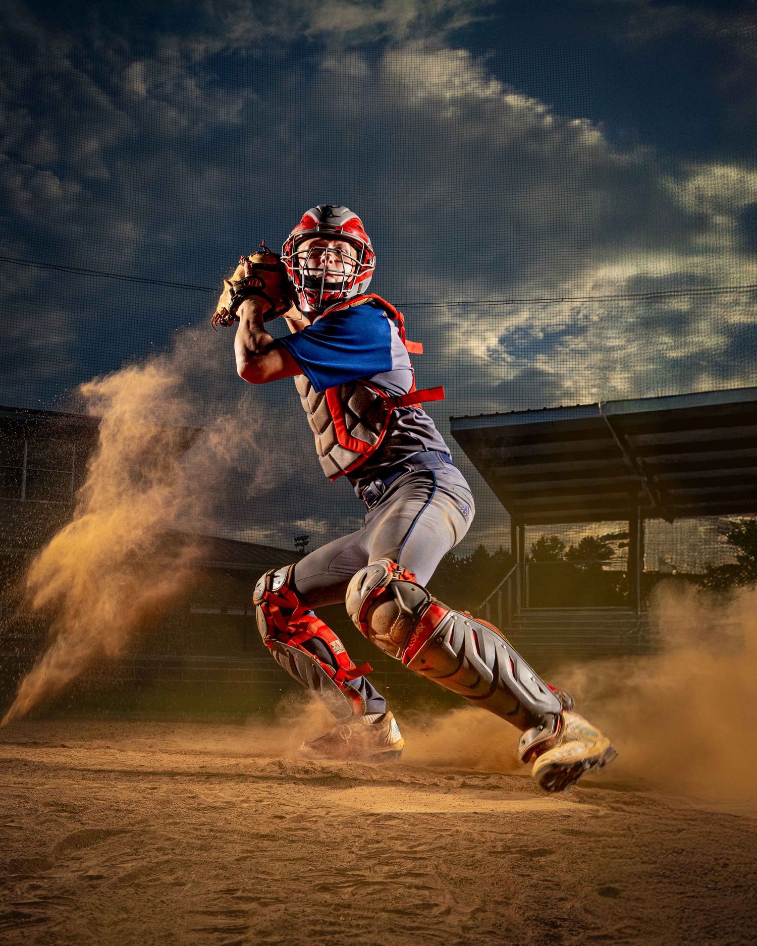 Baseball catcher sliding dramatically in the dirt to make a play during an intense game at sunset.