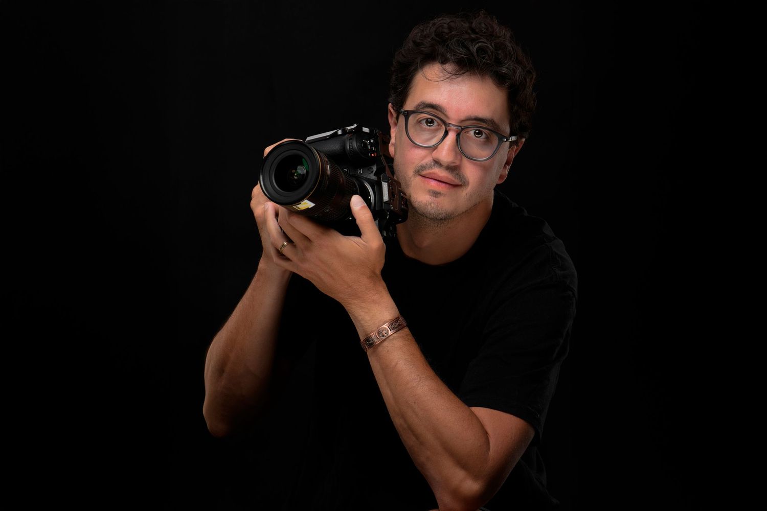 Close-up headshot of young man with glasses and facial hair against white background.