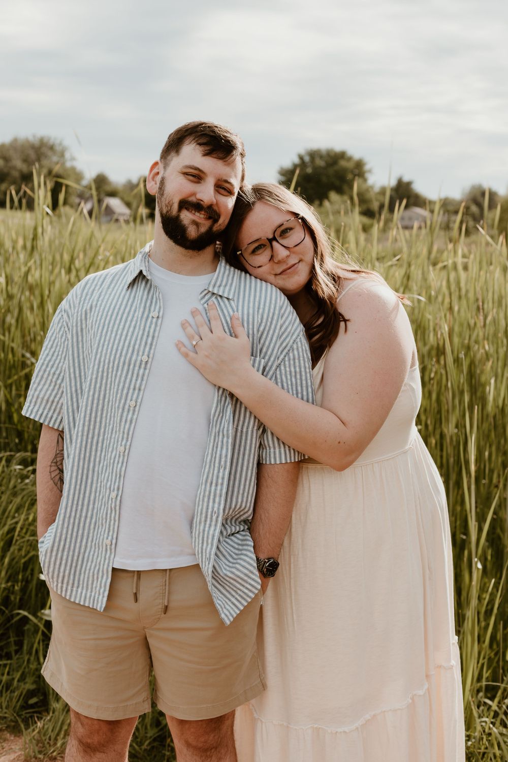 A smiling couple embraces in a green field, the woman in white dress leaning on her partner.