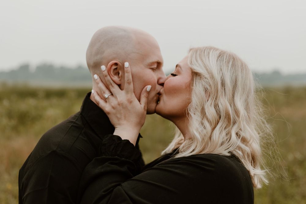 Couple sharing a romantic kiss in an outdoor field during an engagement photo session.