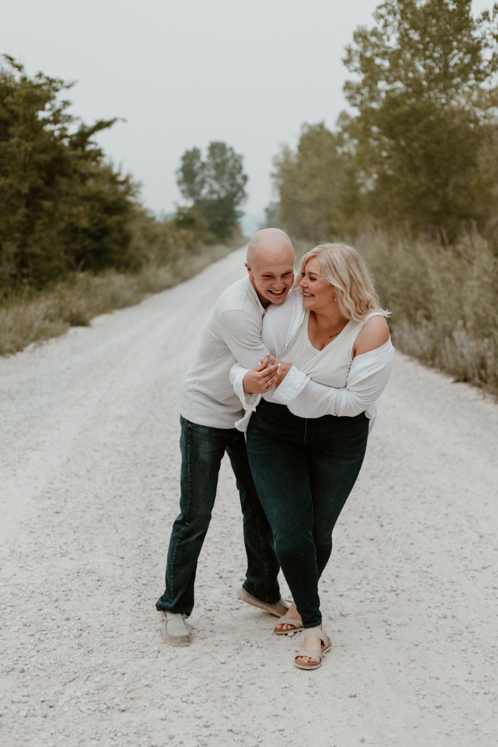 Happy couple laughing and dancing together on a scenic gravel road surrounded by trees.