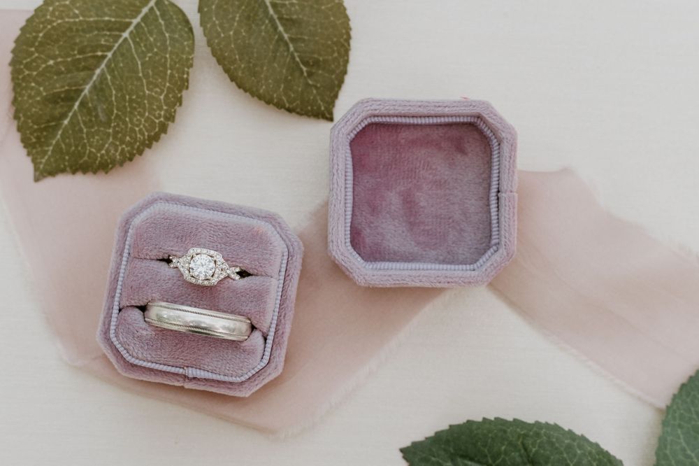 Diamond engagement ring and wedding band displayed in lavender velvet ring box with green leaves.