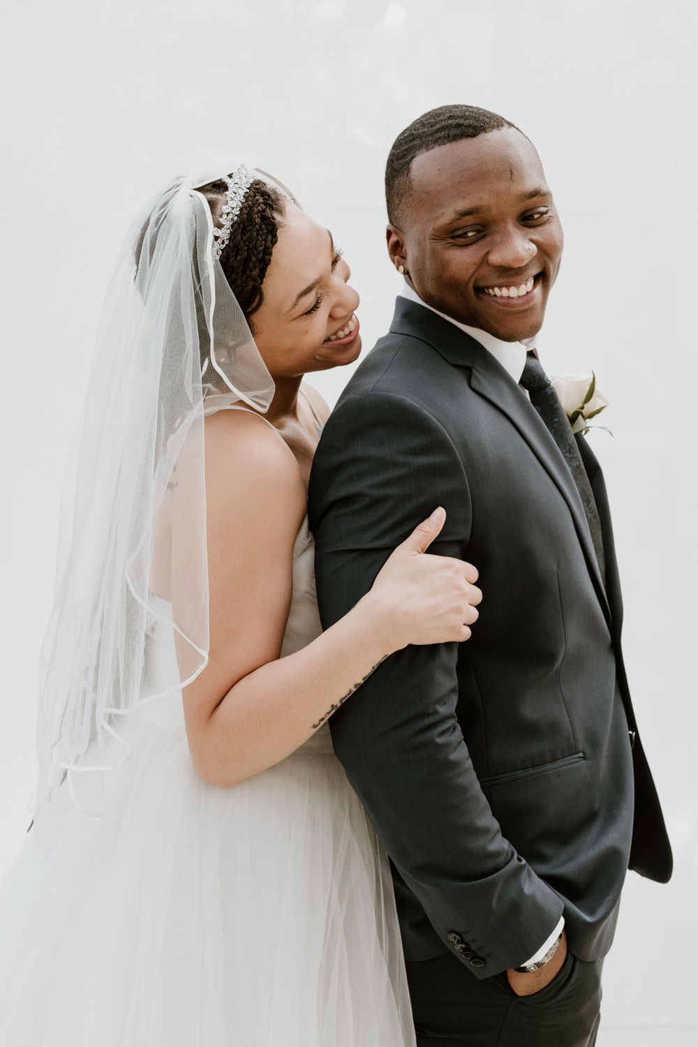 Joyful newlywed couple in wedding attire smiling, bride in veil embracing groom in black suit.