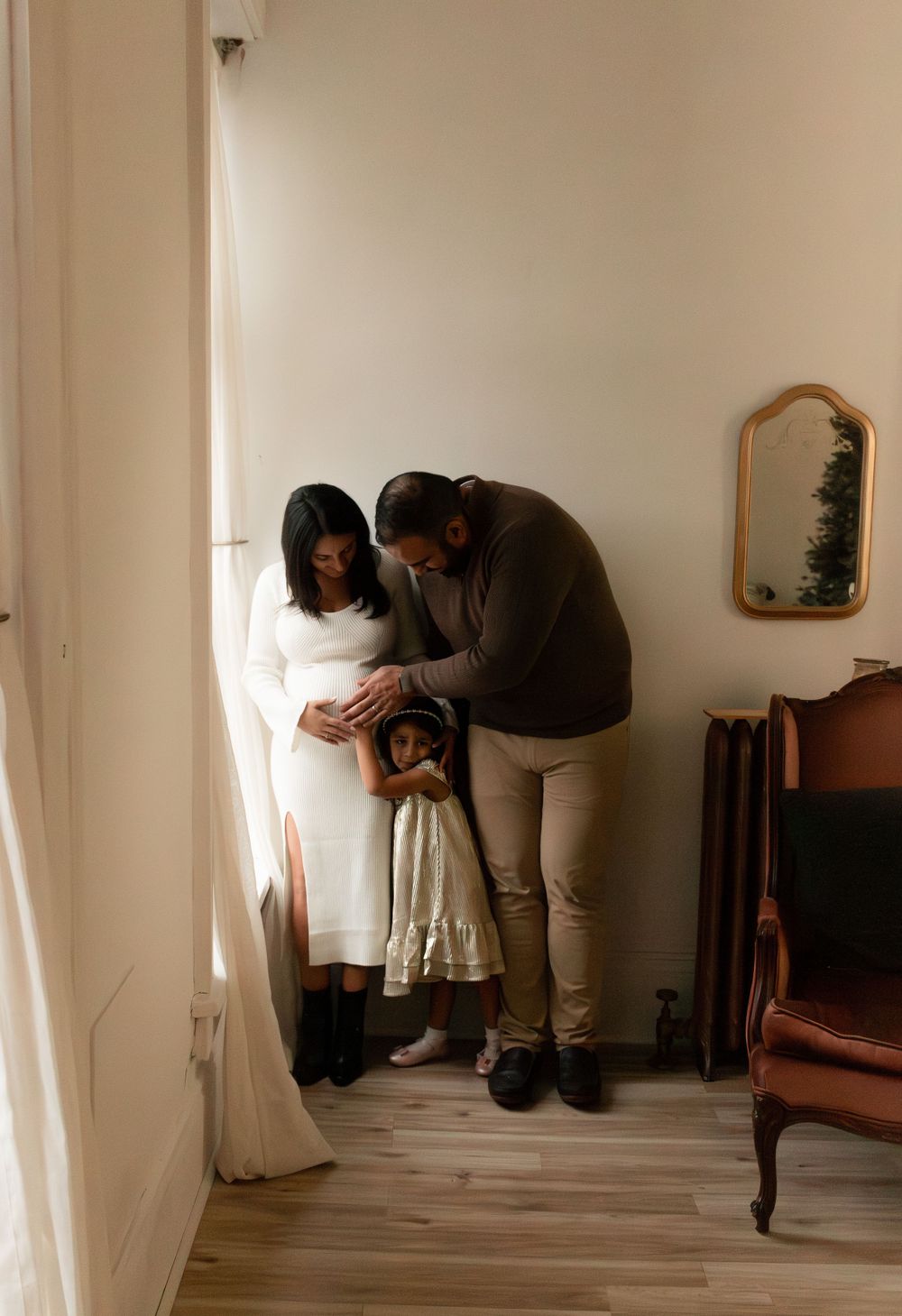 A family shares an intimate moment together in a minimalist room with natural light streaming through curtains.