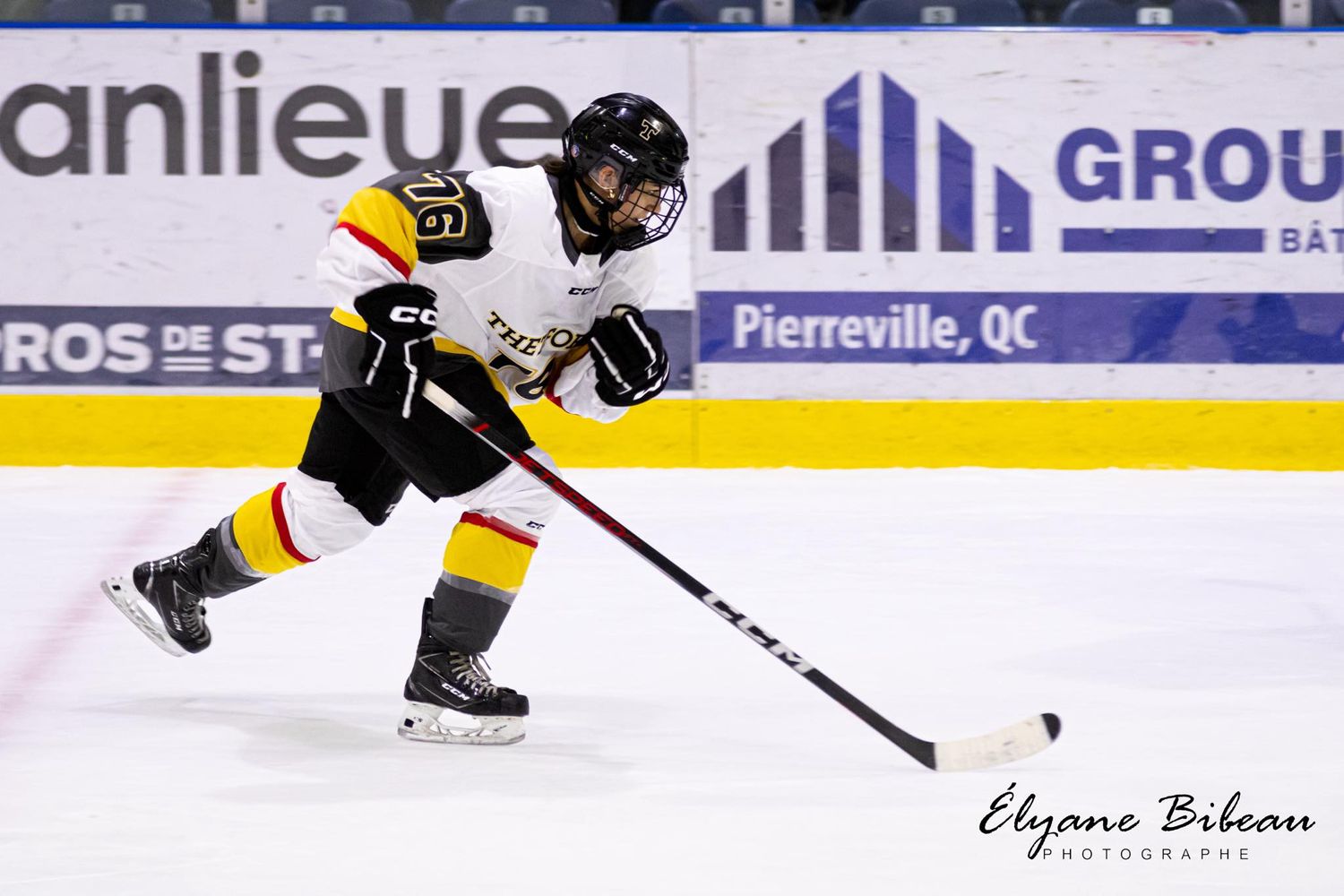 Hockey player in yellow and black uniform skating with puck on ice rink.