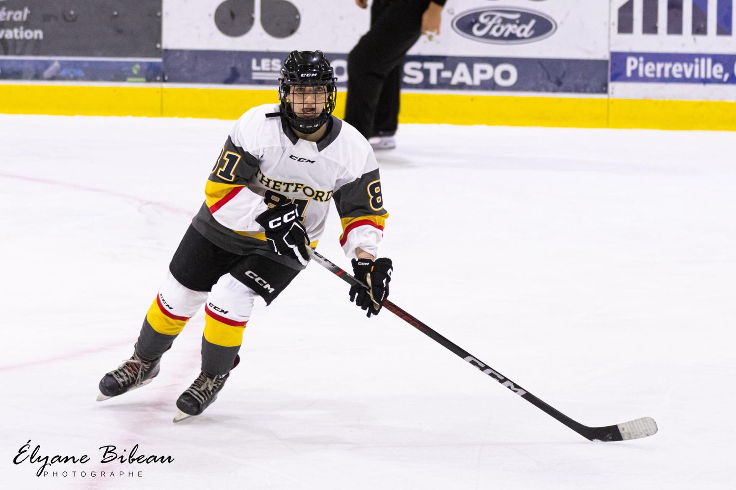 Hockey player in white jersey carrying puck while skating on ice.