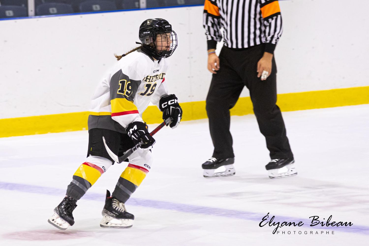 Hockey player skating in yellow and white uniform next to referee on ice rink.