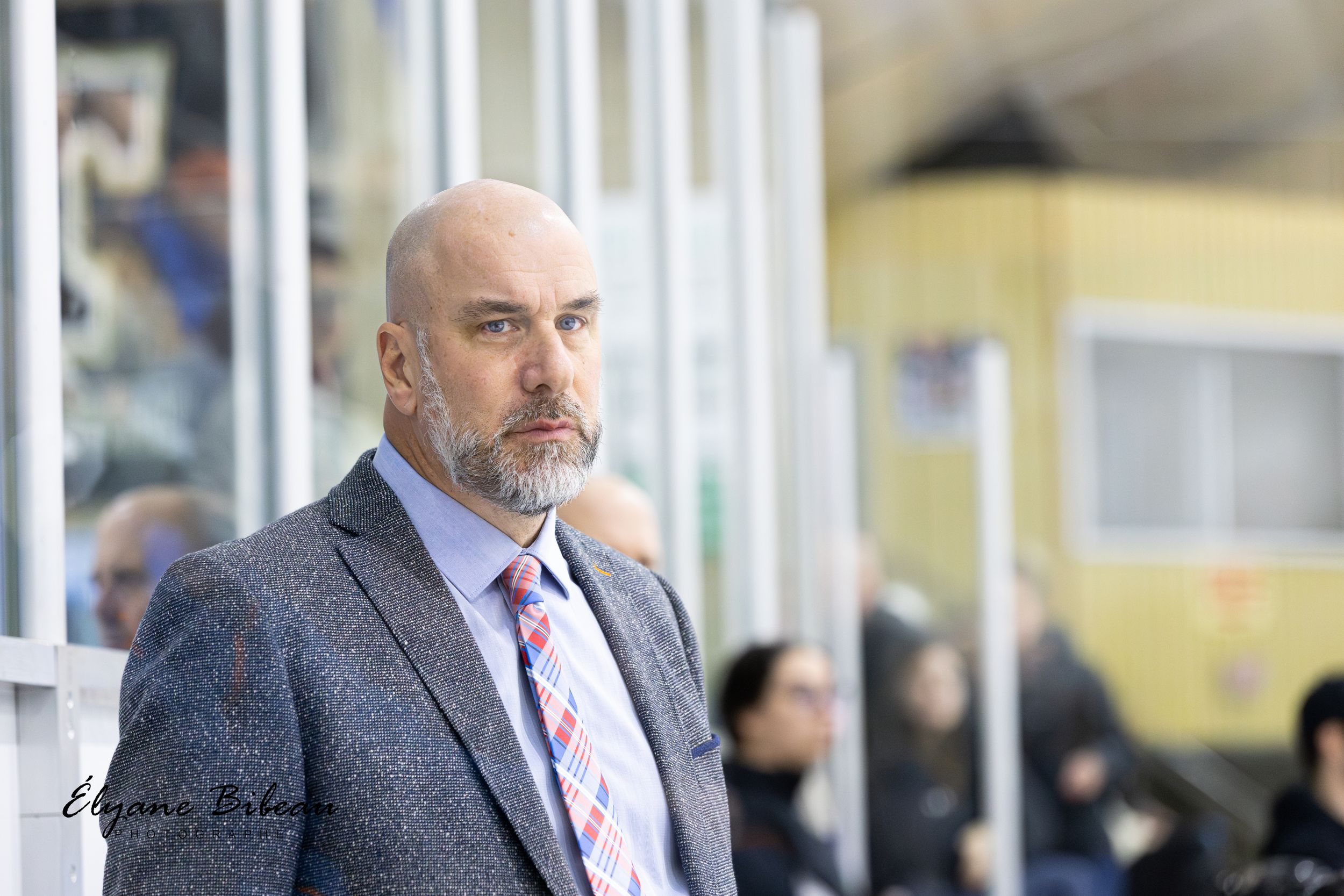 A coach watches intently from behind the glass during an ice hockey game.