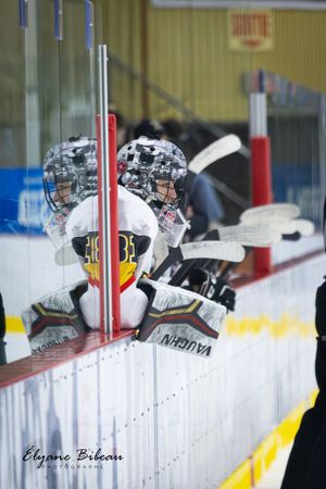 Hockey players in white jerseys watch from the bench during a game.