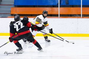 Hockey player in white jersey handles puck while being defended by opponent in black.