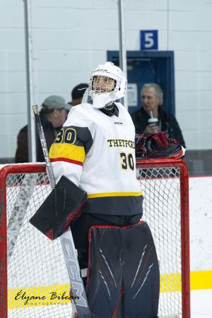Hockey goalie in white and yellow jersey stands in front of net during game.