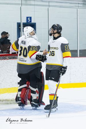Hockey player takes shot while teammate watches from goal during practice.