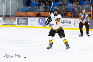 Hockey player in white jersey skates with puck during competitive match.