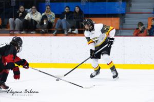 Hockey player in yellow jersey controls puck while opponent defends during ice hockey match.