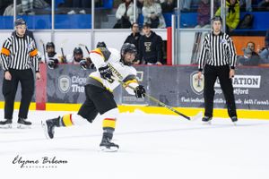 Ice hockey player leaps in mid-air during intense game action with referees watching.