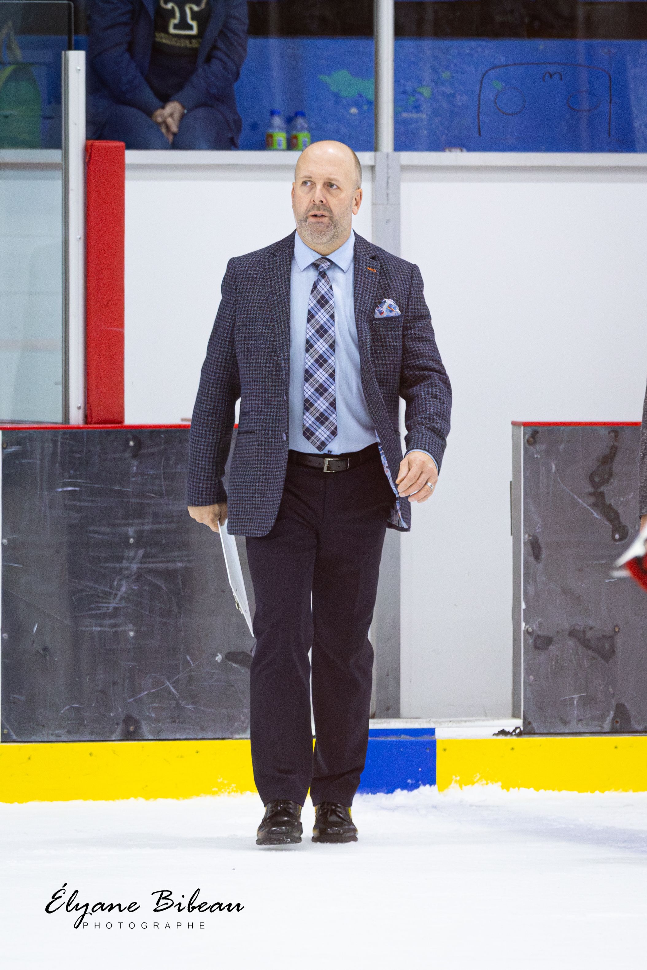 Professional in suit and tie walks along ice rink during hockey event.