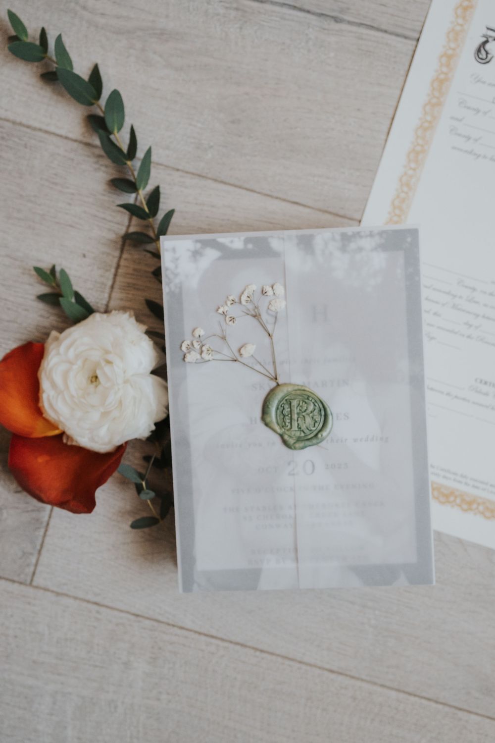 Wedding invitation suite with wax seals and floral elements on white wooden background.