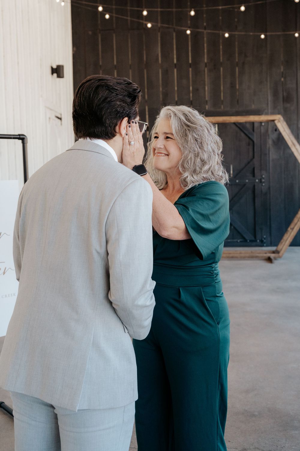 Emotional moment between two people at wedding venue with string lights and wooden backdrop.