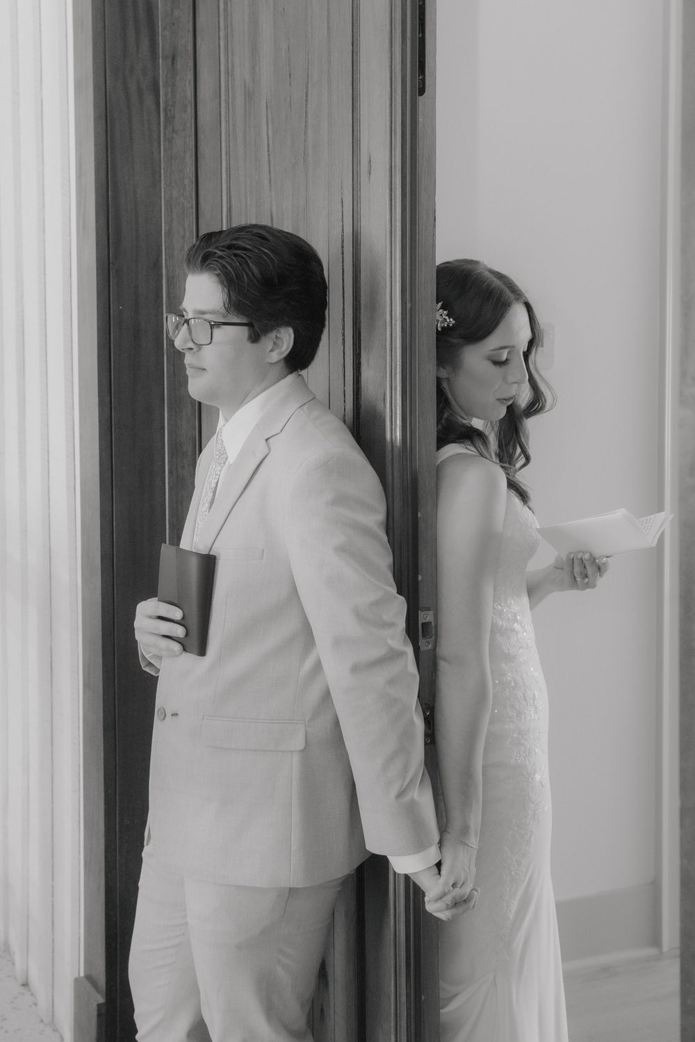 Black and white photos of couple having playful first look moment behind a door.