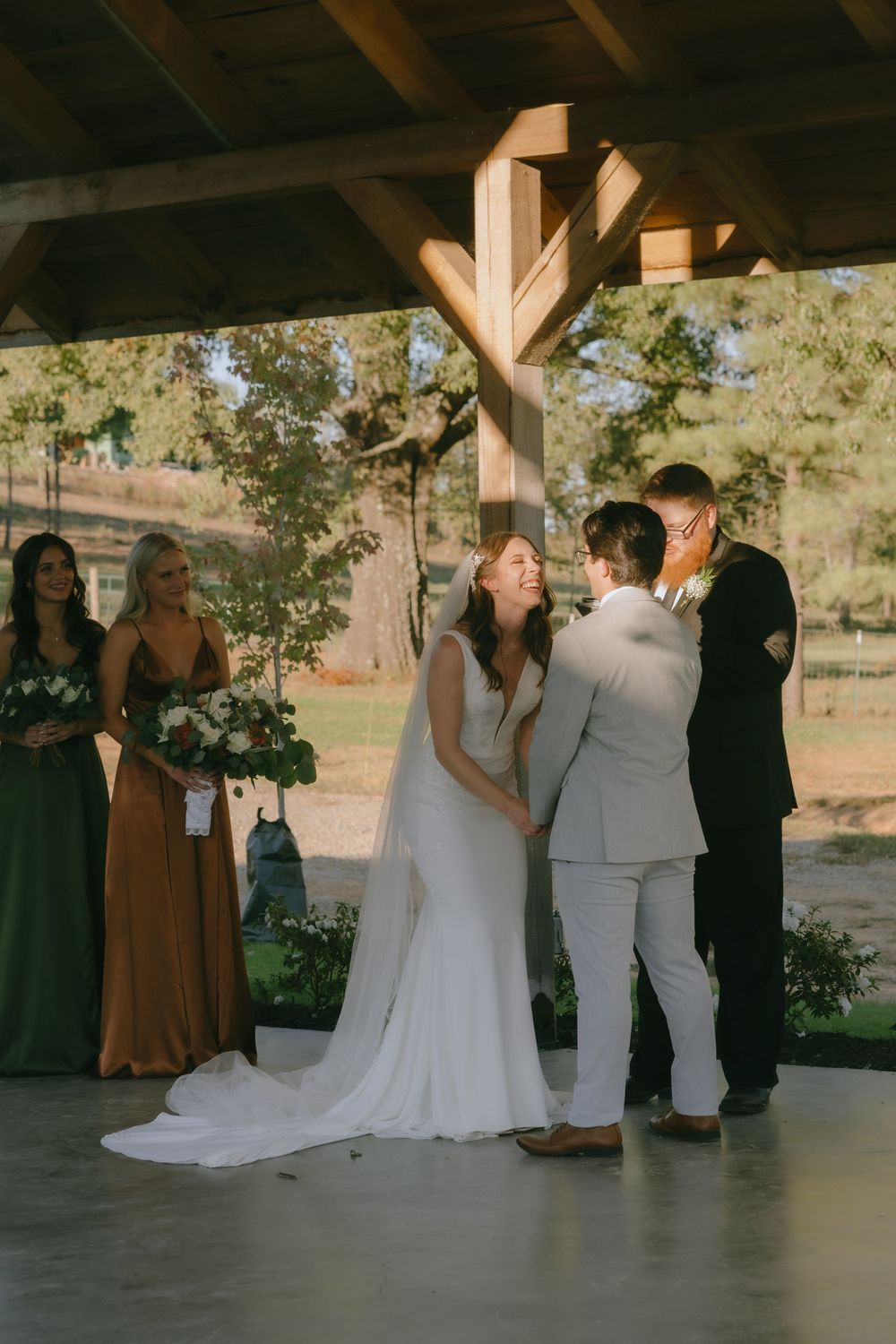 Wedding ceremony under rustic wooden pavilion with guests watching couple's first kiss.