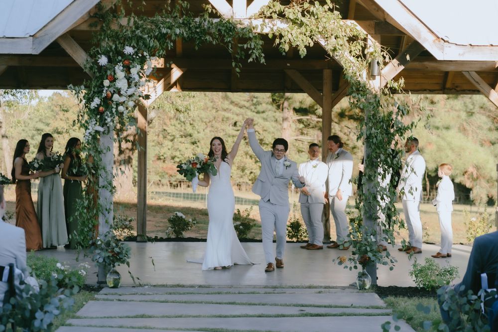 Wedding ceremony site decorated with floral arrangements under wooden pavilion structure.