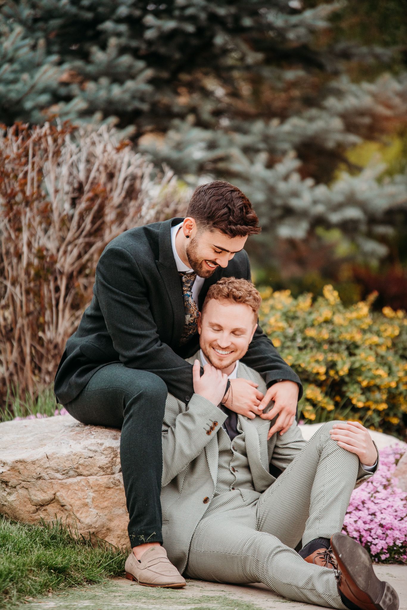 Couple sharing tender embrace while sitting on stone wall in garden setting.