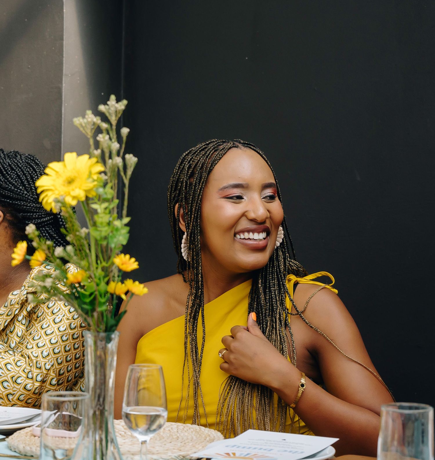 Woman in yellow dress enjoying dinner party with floral decorations.