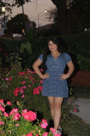 Woman in blue polka dot dress poses by pink flowers in garden at dusk.