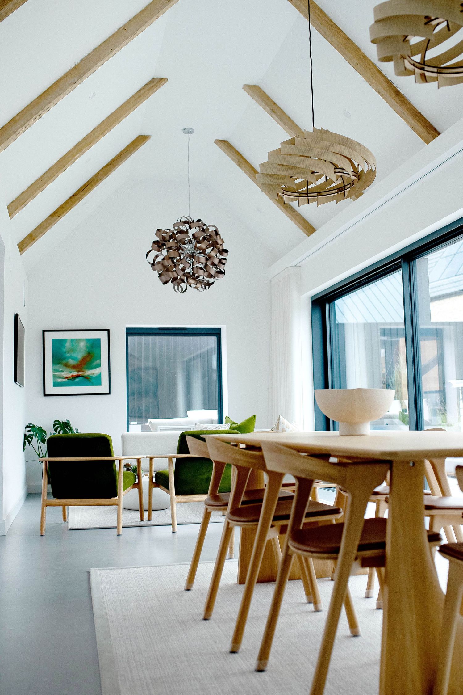 Modern dining room with vaulted ceiling, wooden light fixtures, and Scandinavian-style furniture in a bright airy space.